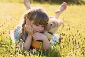 Kleines Mädchen auf einer Wiese mit einem Teddybären