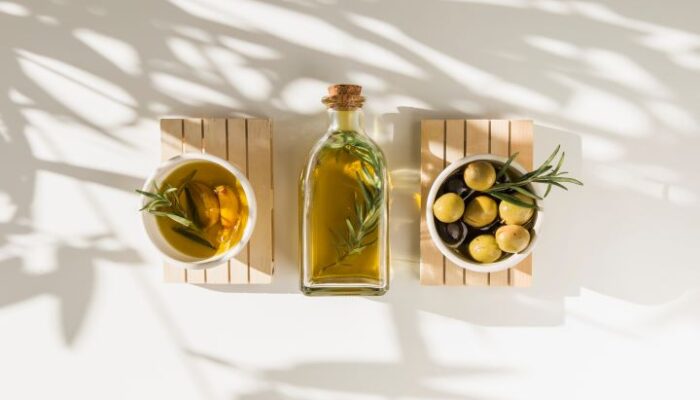 bottiglia di olio e ciotoline con olio e aromi su fondo bianco